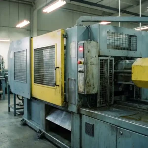 Industriemaschine mit Sicherheitsverkleidungen, gelbem Schutzgitter und rotem Not-Aus-Schalter auf Fabrikboden.